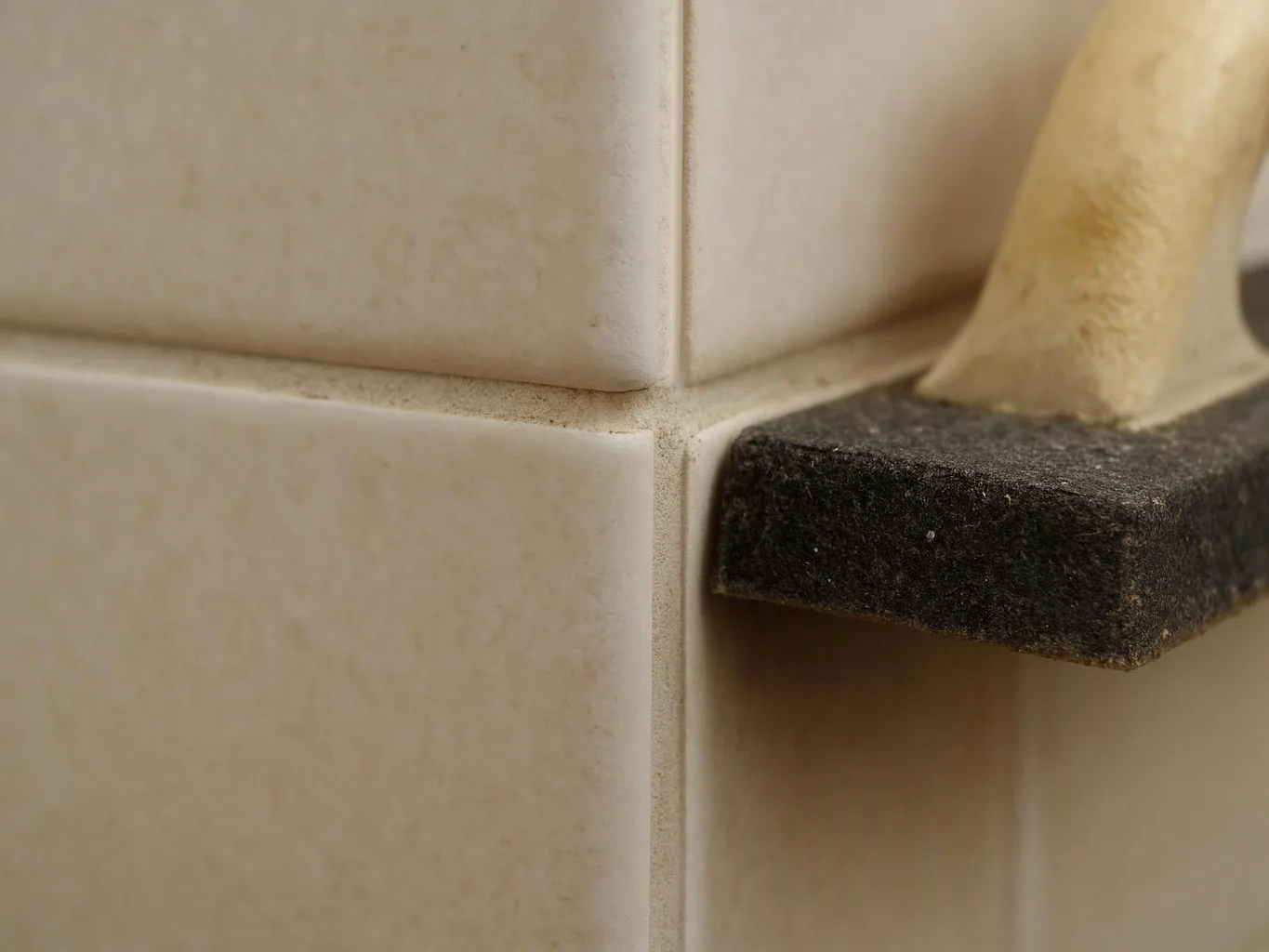 Close-up of dirty beige tiles and a black plastic bracket on a bathroom wall