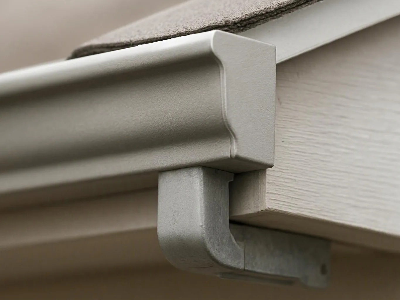 Close-up of a gray gutter corner and downspout fitting attached to a house roofline
