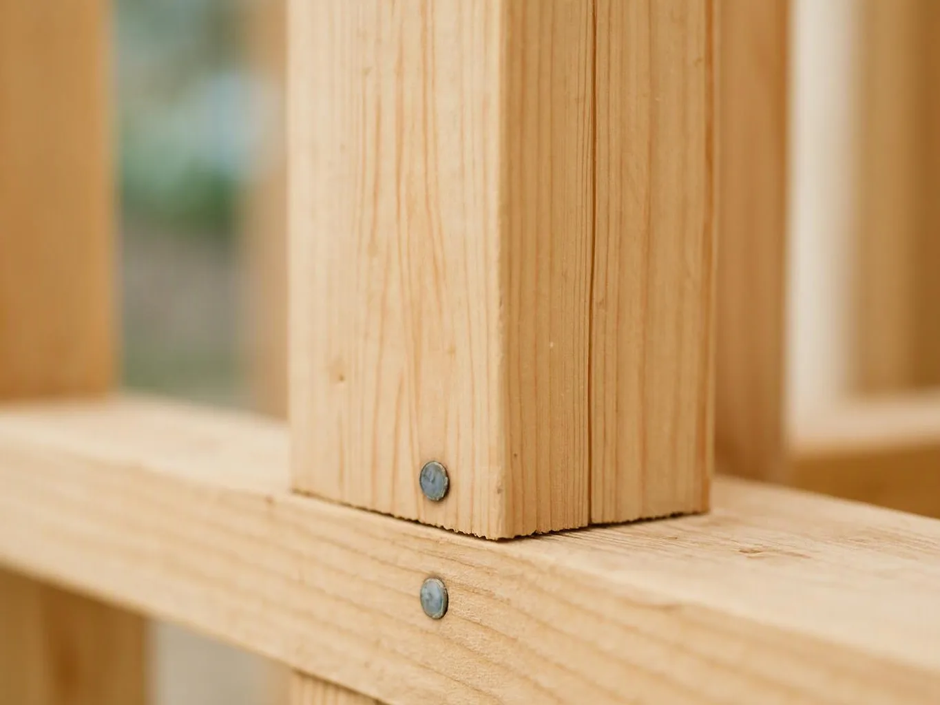 Close-up of pale wooden beams joined with two metal screws in a blurred construction frame