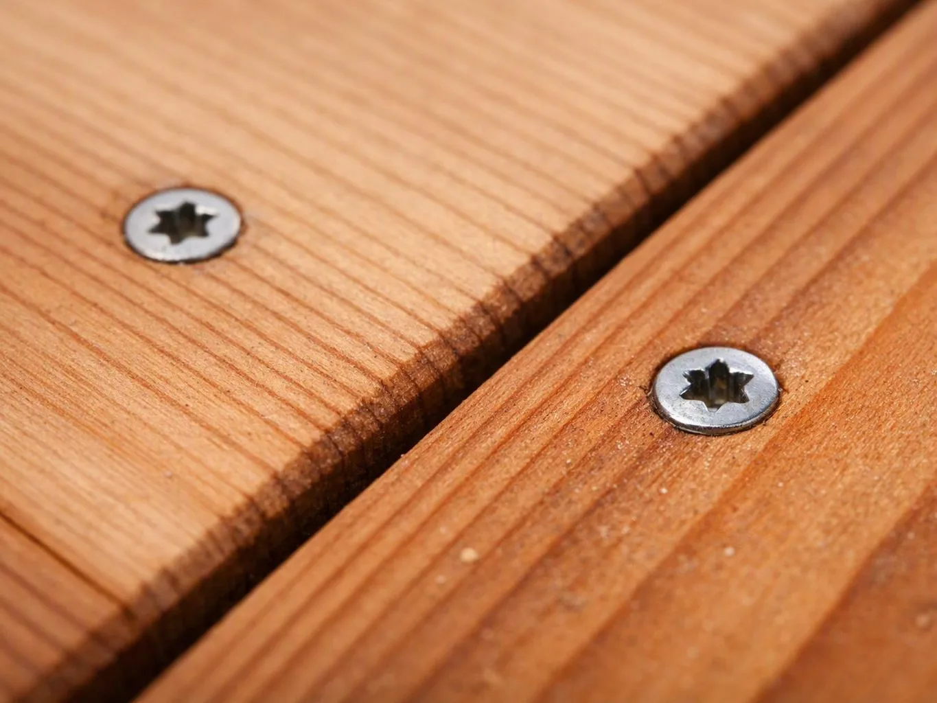 Close-up of two silver screws fastening warm wooden boards with a narrow gap between them