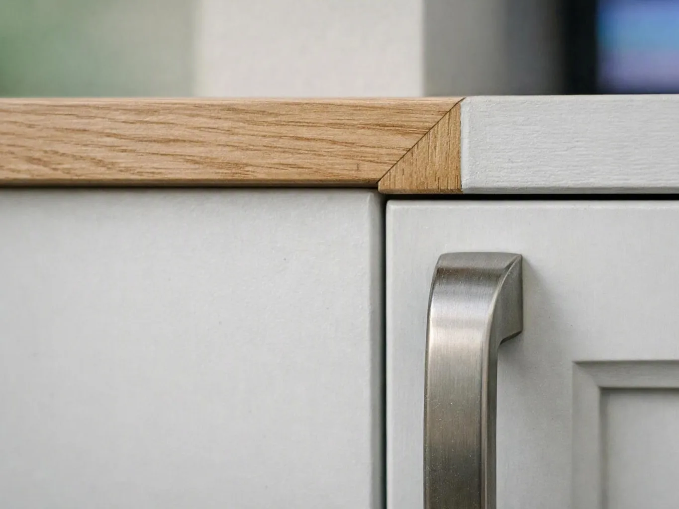 Close-up of a white cabinet door with a brushed metal handle and a light wood countertop edge