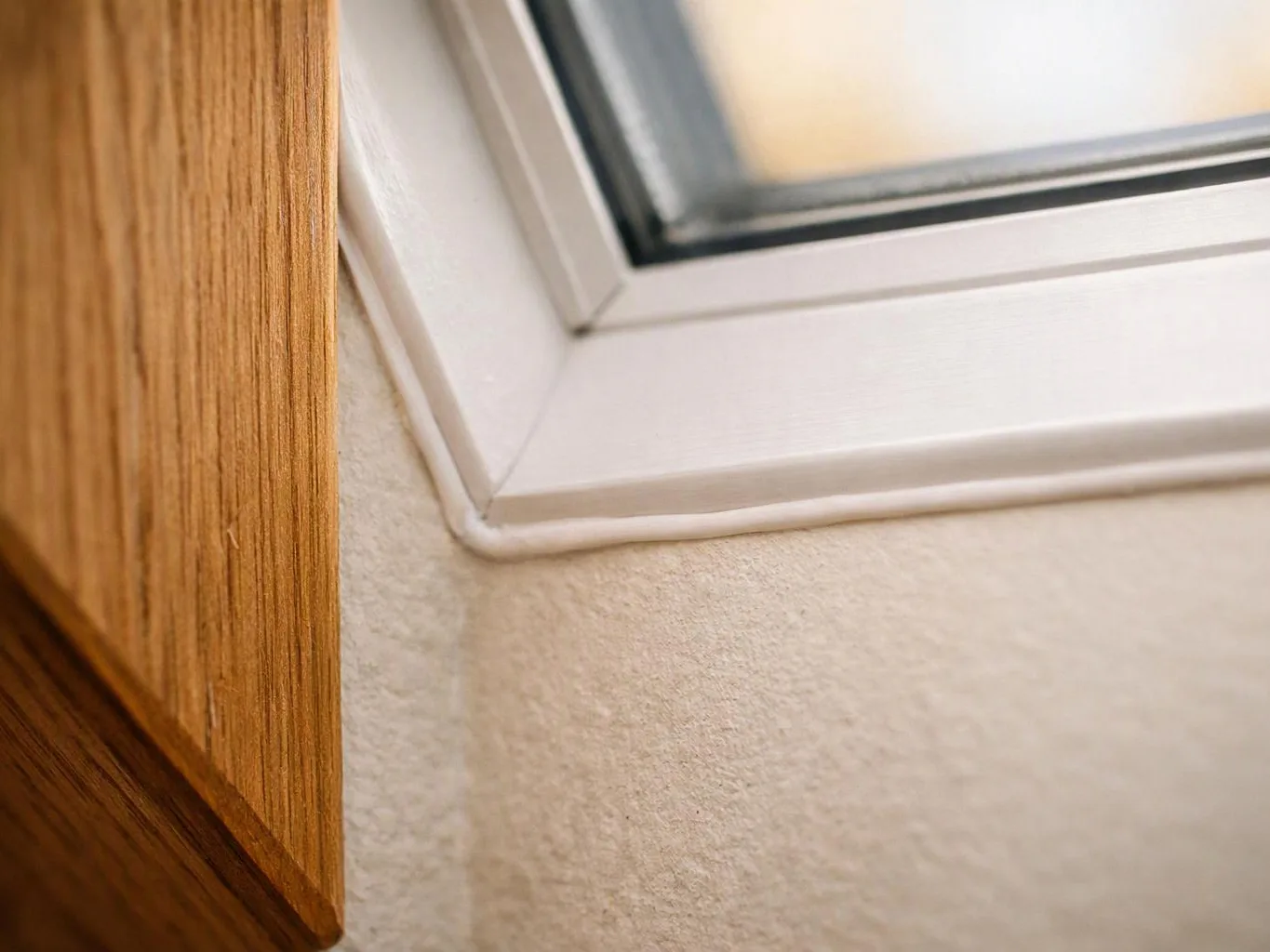 Close-up of a white window frame beside a wood panel and textured wall