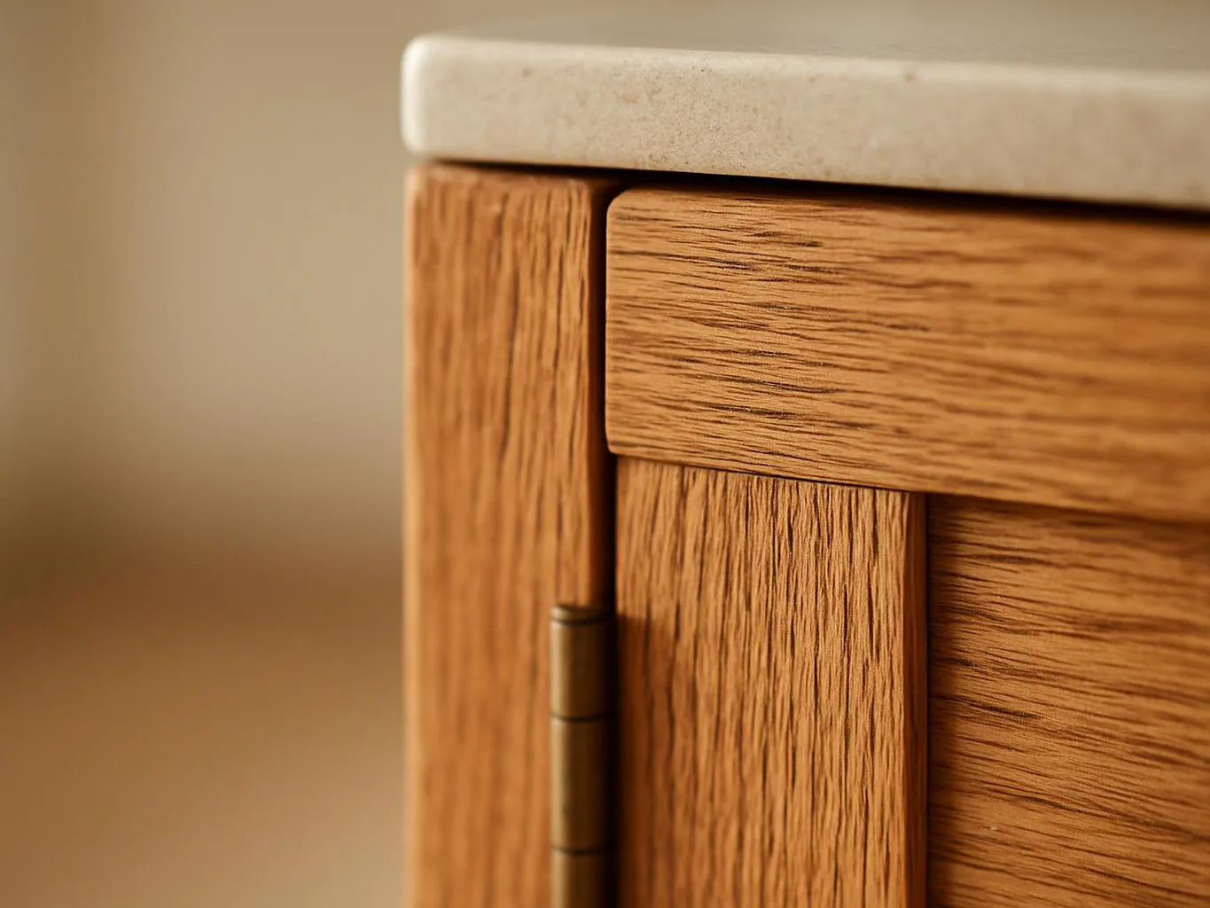 Close-up of a wooden cabinet corner with a brass hinge and a pale stone countertop above