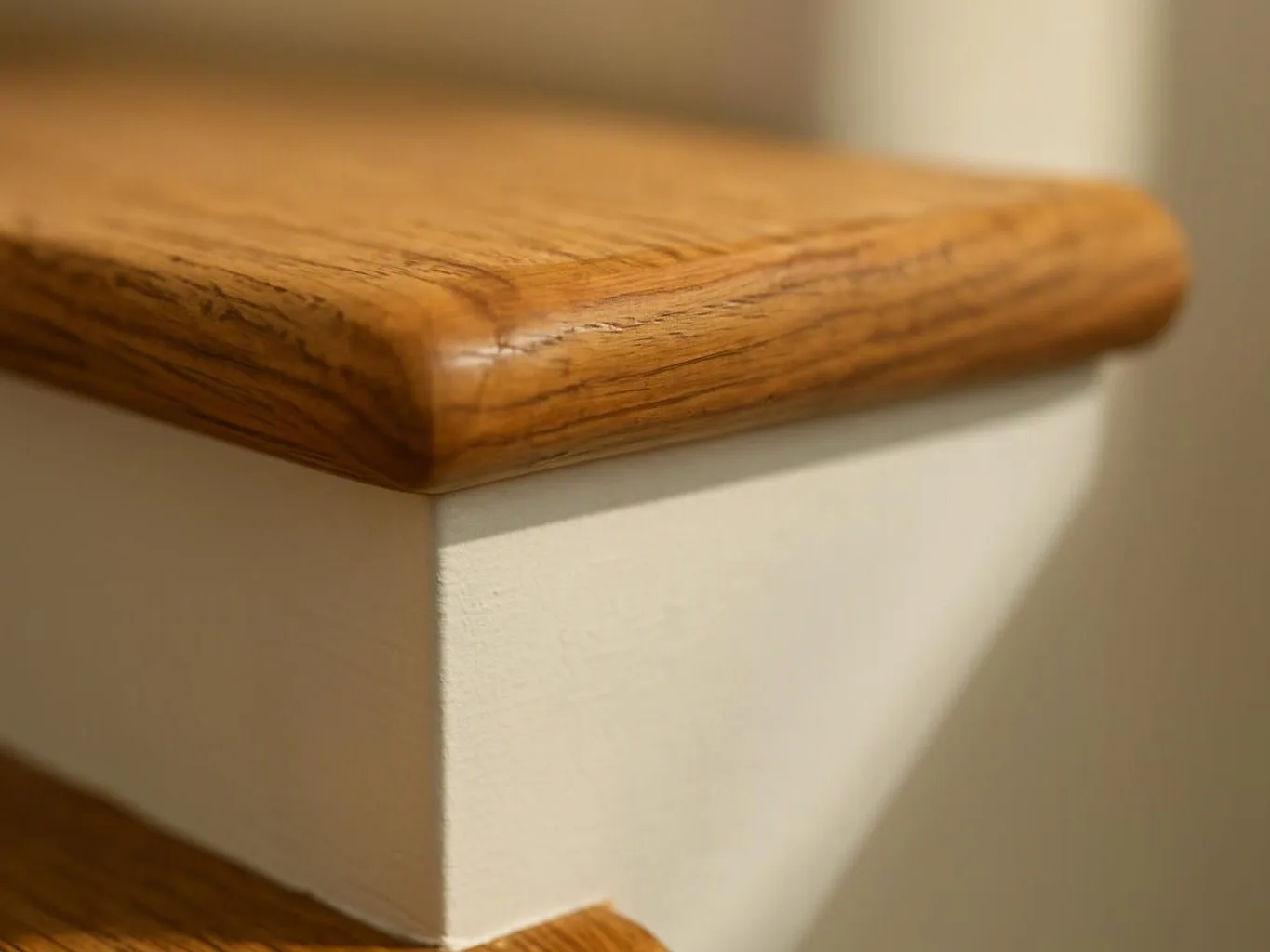 Close-up of a wooden stair tread with a rounded edge above a white painted riser