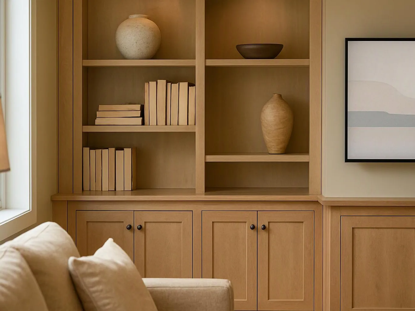 A warm wood bookcase holds books and vases beside a framed print and a beige sofa corner